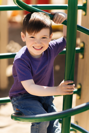 summer, childhood, leisure and people concept - happy little boy on children playground climbing frameの写真素材