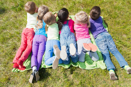 summer, childhood, leisure and people concept - group of happy kids lying on blanket or cover outdoorsの写真素材
