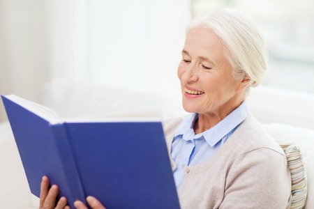age, leisure and people concept - happy smiling senior woman reading book at homeの写真素材