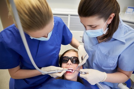 people, medicine, stomatology and health care concept - female dentists with mirror, drill and probe treating patient girl teeth at dental clinic officeの写真素材