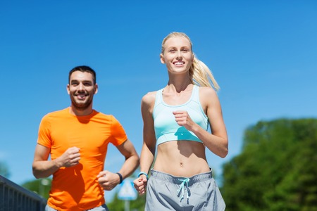 fitness, sport, friendship and healthy lifestyle concept - smiling couple running outdoorsの写真素材