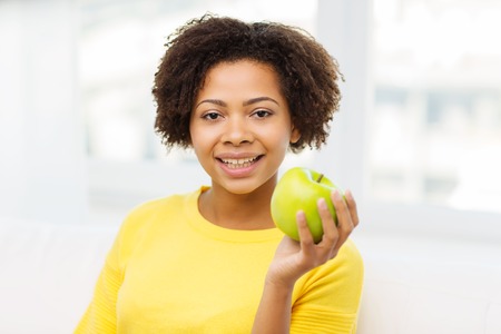 people, food, healthy eating and dental care concept - happy african american young woman with green apple at homeの写真素材