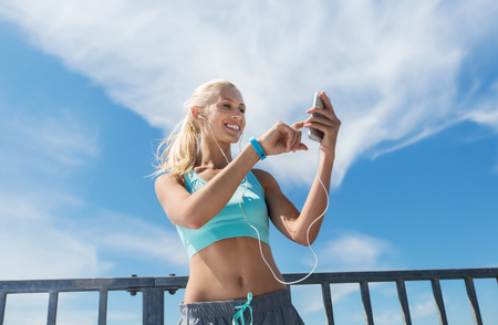 fitness, sport, people, technology and healthy lifestyle concept - smiling young woman with smartphone and earphones listening to music and exercising outdoorsの写真素材