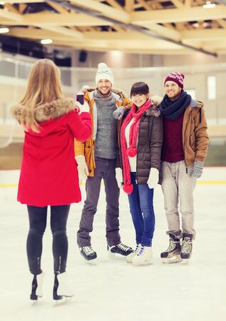 people, friendship, technology and leisure concept - happy friends taking photo with smartphone on skating rinkの写真素材