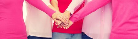 healthcare, people, gesture, breast cancer awareness and medicine concept - close up of women in pink shirts putting hands on top over white backgroundの写真素材