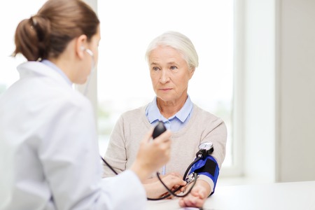 medicine, age, health care and people concept - doctor with tonometer checking senior woman blood pressure level at hospitalの写真素材