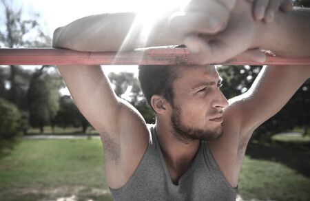 fitness, sport, training and lifestyle concept - young man exercising on horizontal bar outdoors