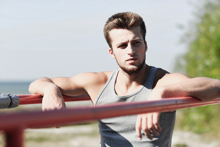 fitness, sport, training and lifestyle concept - young man exercising on parallel bars outdoors