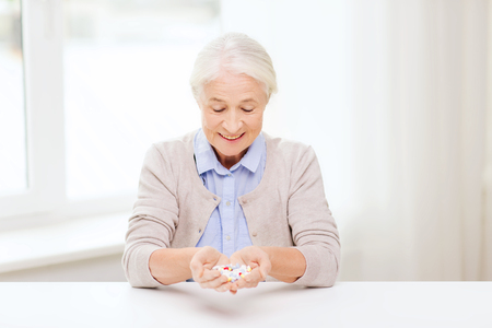 age, medicine, health care and people concept - happy senior woman with pills at home or hospital officeの写真素材