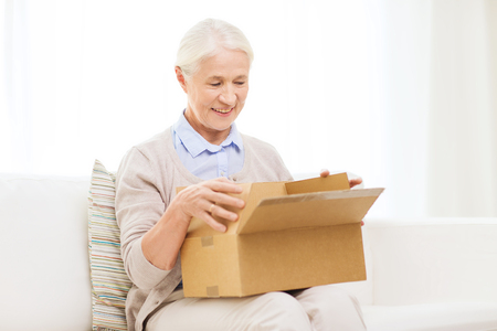 age, delivery, mail, shipping and people concept - happy smiling senior woman looking into open parcel box at homeの写真素材
