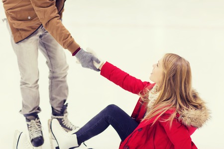 people, friendship, sport and leisure concept - smiling man helping women to rise up on skating rinkの写真素材