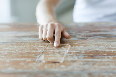business, technology and people concept - close up of woman hand holding and showing transparent smartphone at homeの写真素材