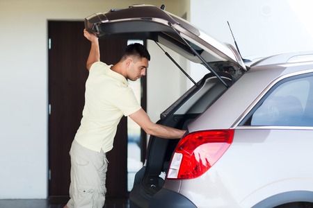 road trip, transport, private property leisure and people concept - young man with open car trunk at parking spaceの写真素材