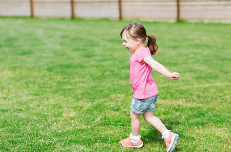 summer, childhood, leisure and people concept - happy little girl running on green summer fieldの写真素材