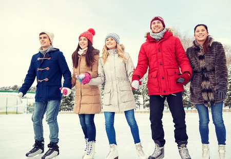 people, winter, friendship, sport and leisure concept - happy friends ice skating on rink outdoorsの写真素材