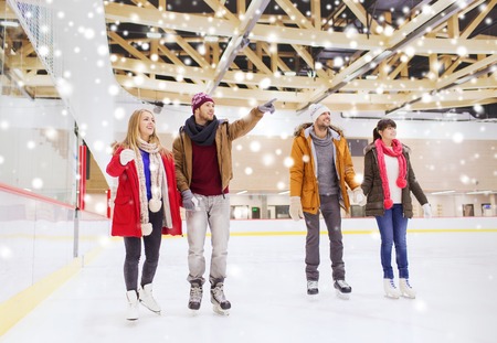 people, friendship, sport, gesture and leisure concept - happy friends pointing finger on skating rinkの写真素材