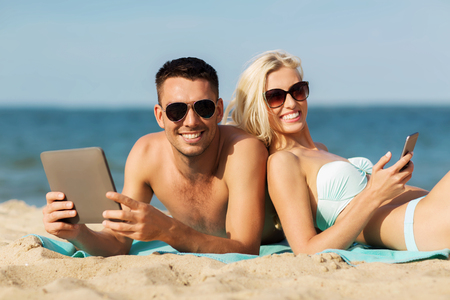 love, travel, tourism, technology and people concept - happy couple on vacation with tablet pc computer sunbathing on summer beachの写真素材