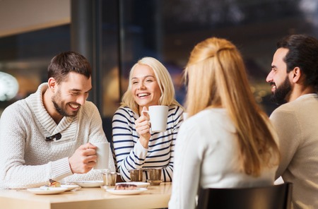 people, leisure and communication concept - happy friends meeting and drinking tea or coffee at cafe