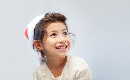 christmas, holidays, childhood and people concept - happy little girl in santa hat over gray backgroundの写真素材