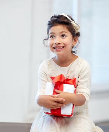 holidays, presents, christmas, childhood and people concept - smiling little girl with gift box at homeの写真素材