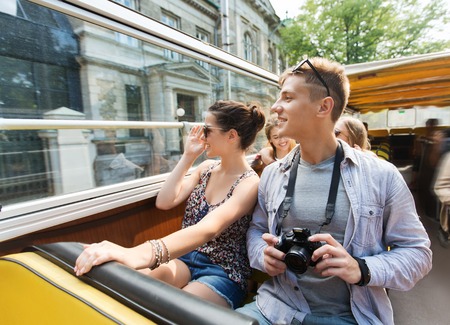 travel, tourism, summer vacation, sightseeing and people concept - smiling teenage couple with camera traveling by tour busの写真素材