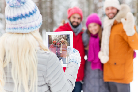 technology, season, friendship and people concept - close up of happy men and women taking picture with tablet pc computer in winter forestの写真素材