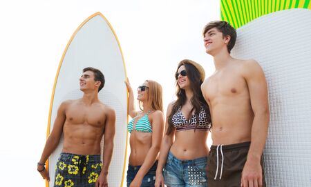 friendship, sea, summer vacation, water sport and people concept - group of smiling friends wearing swimwear and sunglasses with surfboards on beachの写真素材