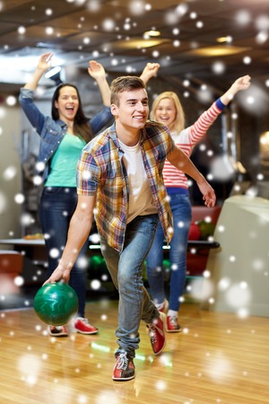 people, leisure, sport and entertainment concept - happy young man throwing ball in bowling club at winter seasonの写真素材