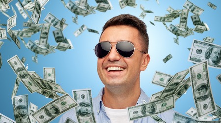 business, finance, success and people concept - face of smiling middle aged latin man in shirt and sunglasses over blue background with heap of falling dollar moneyの写真素材