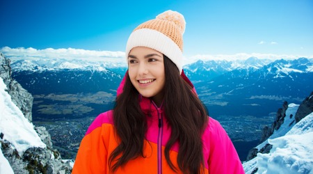 winter, leisure, clothing and people concept - happy young woman or teenage girl in winter clothes outdoors over snowy mountains backgroundの写真素材