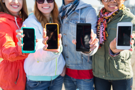 people, friendship, cloud computing, advertising and technology concept - close up of happy teenage friends showing blank smartphone screens outdoorsの写真素材