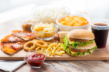 fast food and unhealthy eating concept - close up of hamburger or cheeseburger, deep-fried squid rings, french fries, drink and ketchup on wooden table