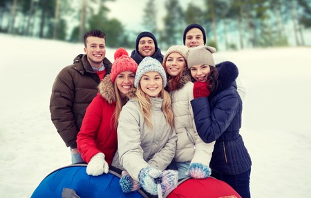 winter, leisure, friendship, technology and people concept - group of smiling young men and women with snow tubes taking picture with smartphone selfie stick outdoorsの写真素材