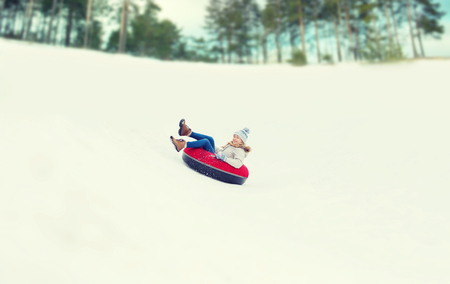 winter, leisure, sport, and people concept - happy teenage girl or woman sliding down on snow tubeの写真素材