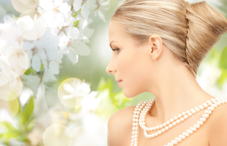 beauty, luxury, people, holidays and jewelry concept - beautiful woman with sea pearl necklace or beads over cherry blossom backgroundの写真素材