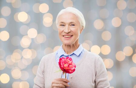 age, holidays and people concept - happy smiling senior woman with flower over holidays lights backgroundの写真素材
