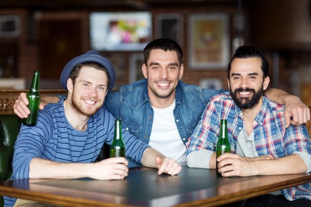 people, leisure, friendship and bachelor party concept - happy male friends drinking bottled beer and hugging at bar or pub