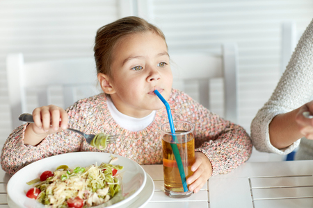 childhood, food and people concept - little girl eating pasta and drinking apple juice for dinner at restaurant or cafeの写真素材