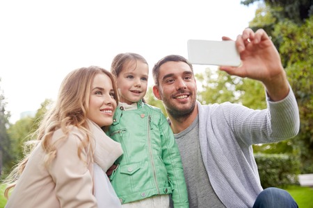 family, childhood, technology and people concept - happy father, mother and little daughter taking...