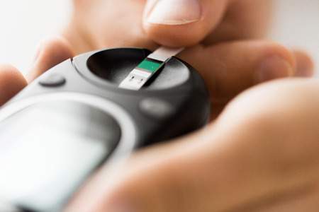 medicine, diabetes, glycemia, health care and people concept - close up of man checking blood sugar level by glucometer and test stripe at homeの写真素材
