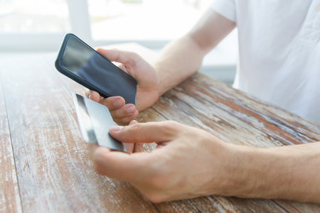 business, technology, cash free and internet people concept - close up of male hands holding smart phone and credit card on wooden tableの写真素材
