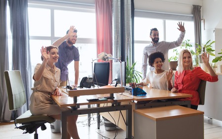 business, startup and office concept - happy creative team waving hands in officeの写真素材