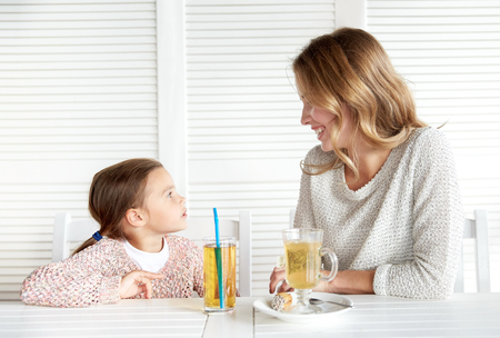 family, parenthood, communication and people concept - happy mother and little girl having dinner and talking at restaurant or cafeの写真素材