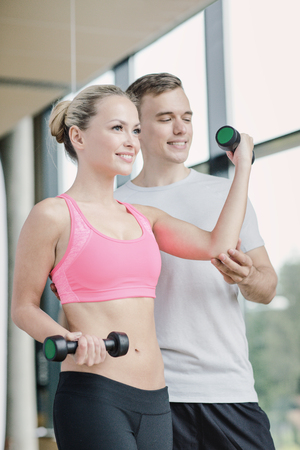 fitness, sport, exercising and diet concept - smiling young woman and personal trainer with dumbbells in gymの写真素材