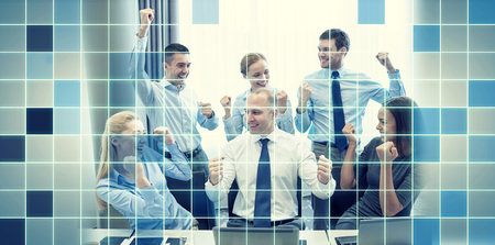 business, people, technology, gesture and teamwork concept - smiling business team raising hands and celebrating victory in office over blue squared grid backgroundの写真素材