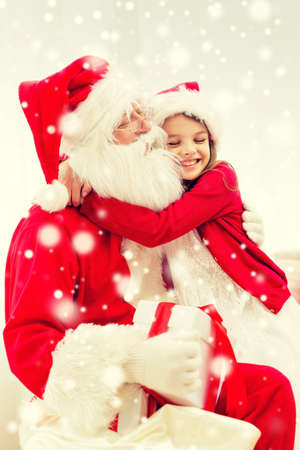 holidays, christmas, happiness and people concept - smiling girl with gift box embracing santa claus at homeの写真素材