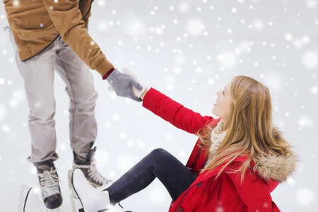 people, friendship, sport and leisure concept - smiling man helping women to rise up on skating rinkの写真素材
