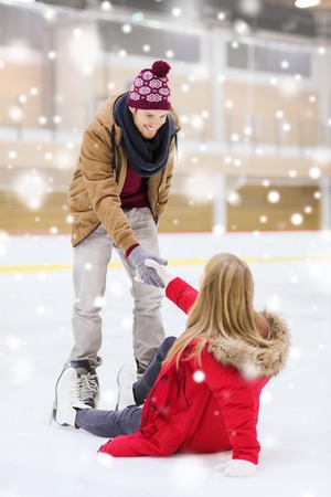 people, friendship, sport and leisure concept - smiling man helping women to rise up on skating rinkの写真素材