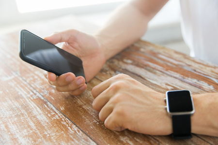 business, technology and people concept - close up of male hand holding smart phone and wearing watch at homeの写真素材