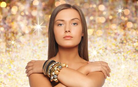 beauty, luxury, people, holidays and jewelry concept - beautiful woman with bracelets over golden lights backgroundの写真素材